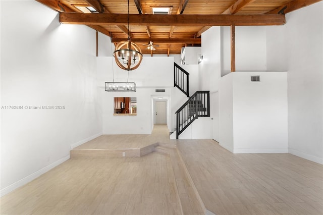 unfurnished living room featuring stairway, wood finished floors, an inviting chandelier, wooden ceiling, and beamed ceiling