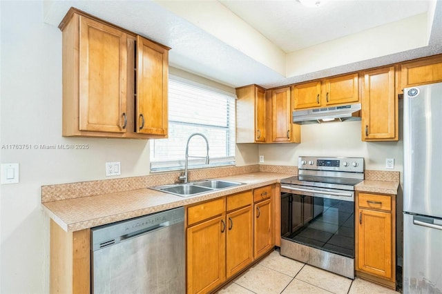 kitchen with brown cabinets, under cabinet range hood, a sink, appliances with stainless steel finishes, and light countertops