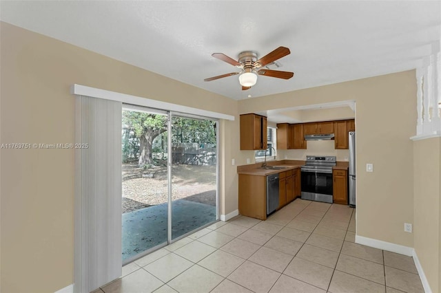 kitchen featuring a ceiling fan, a sink, under cabinet range hood, appliances with stainless steel finishes, and brown cabinets