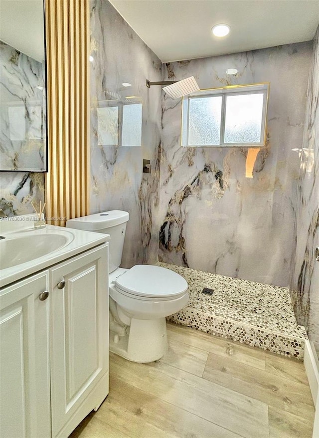 bathroom with a marble finish shower, toilet, wood finished floors, and vanity