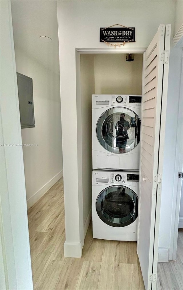 clothes washing area with electric panel, wood finished floors, stacked washing maching and dryer, baseboards, and laundry area