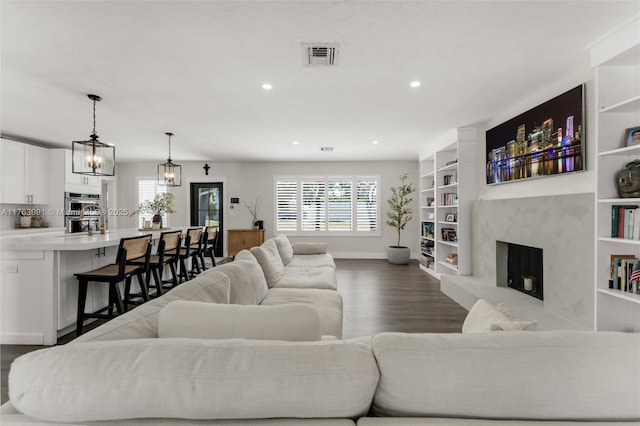 living area featuring built in shelves, baseboards, dark wood finished floors, recessed lighting, and a high end fireplace