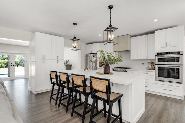 kitchen with a center island with sink, wood finished floors, white cabinetry, stainless steel appliances, and light countertops