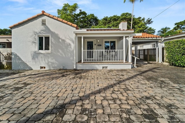 back of property with stucco siding, a porch, a chimney, and fence