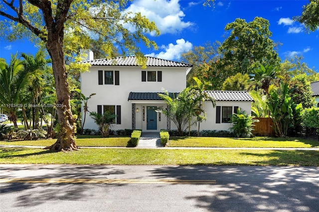 view of front facade with a front lawn, a tiled roof, stucco siding, and fence