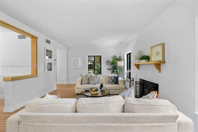 living area featuring a warm lit fireplace, visible vents, wood finished floors, and baseboards