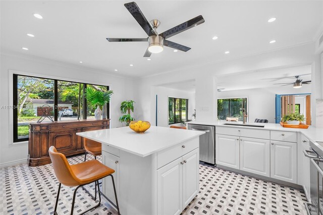 kitchen featuring light countertops, stainless steel dishwasher, a kitchen island, white cabinets, and a ceiling fan