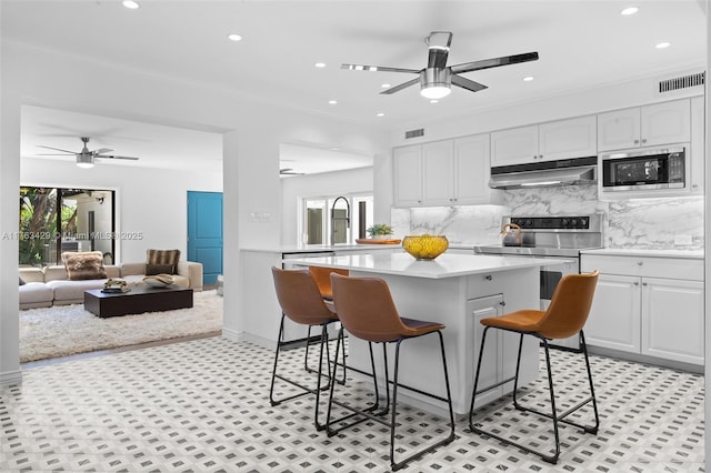 kitchen featuring visible vents, ceiling fan, stainless steel microwave, under cabinet range hood, and range with electric cooktop