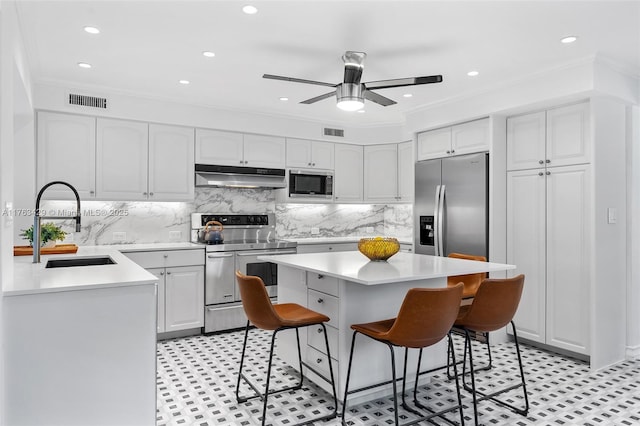kitchen featuring visible vents, appliances with stainless steel finishes, under cabinet range hood, a sink, and a breakfast bar area