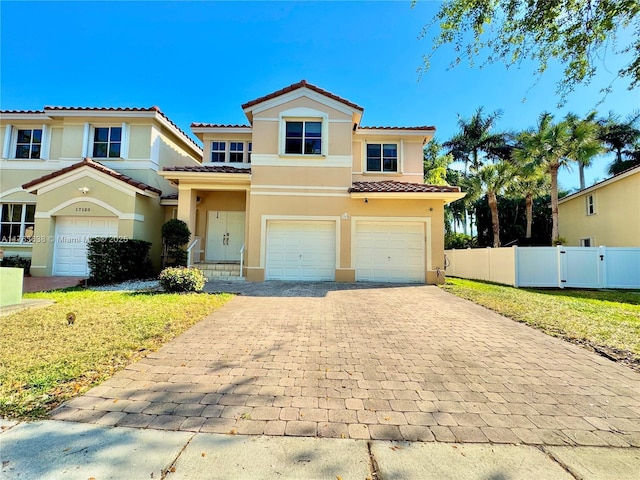 mediterranean / spanish-style home with stucco siding, decorative driveway, fence, an attached garage, and a tiled roof