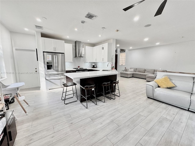 kitchen with visible vents, stainless steel refrigerator with ice dispenser, a kitchen breakfast bar, wall chimney exhaust hood, and open floor plan