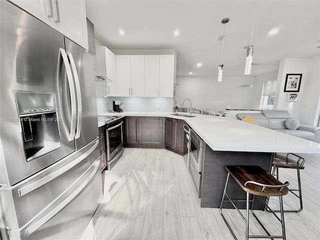 kitchen featuring a peninsula, a sink, stainless steel appliances, a kitchen breakfast bar, and tasteful backsplash