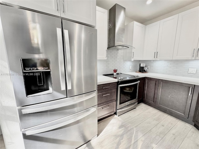 kitchen with wall chimney range hood, backsplash, appliances with stainless steel finishes, white cabinets, and light countertops