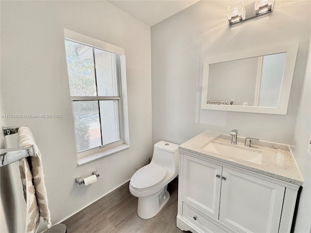 half bath with a wealth of natural light, toilet, vanity, and wood finished floors