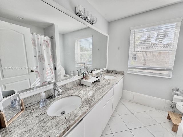 bathroom featuring a sink, baseboards, toilet, and double vanity