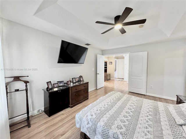 bedroom with a tray ceiling, baseboards, and light wood-style flooring