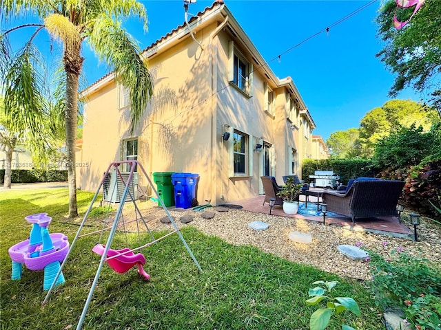 back of property featuring a patio, a lawn, a tile roof, and stucco siding