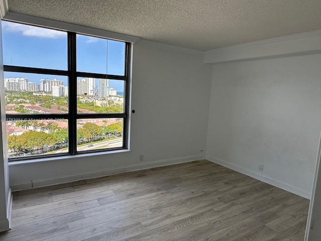 spare room with a view of city, wood finished floors, baseboards, and a textured ceiling