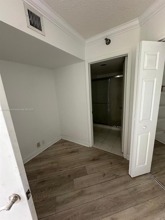 hall with visible vents, a textured ceiling, crown molding, and wood finished floors