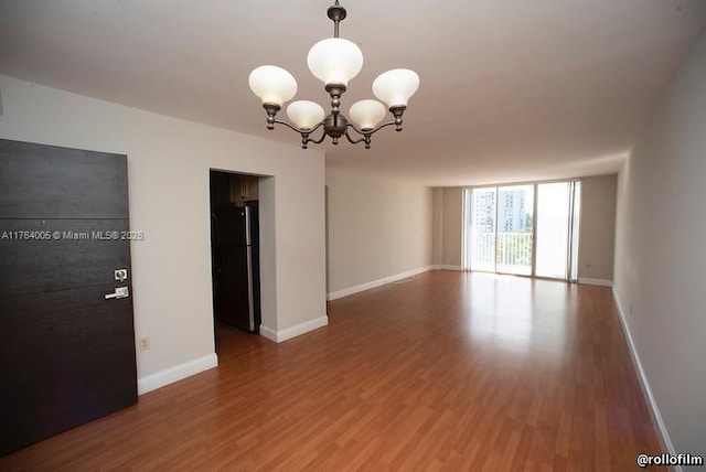 unfurnished room with a wall of windows, a notable chandelier, wood finished floors, and baseboards