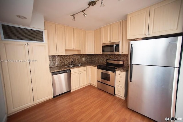 kitchen with a sink, tasteful backsplash, stainless steel appliances, dark stone counters, and light wood finished floors