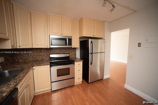 kitchen featuring baseboards, a sink, stainless steel appliances, light wood-style floors, and tasteful backsplash