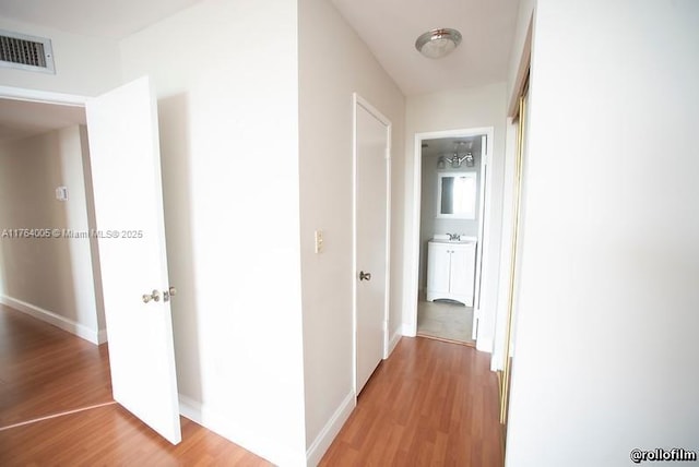 corridor with a sink, visible vents, baseboards, and light wood-style floors