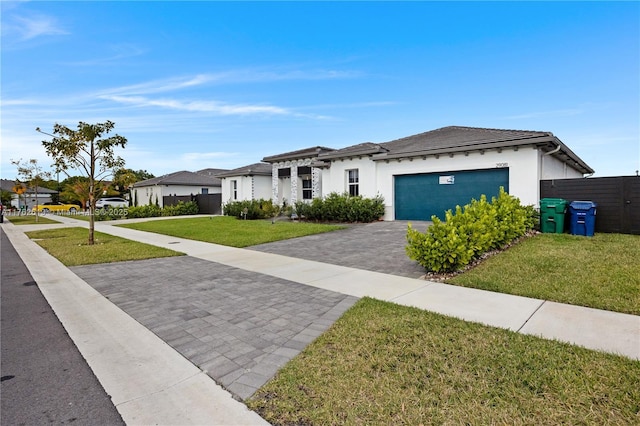 view of front of house with a front yard, fence, an attached garage, stucco siding, and decorative driveway