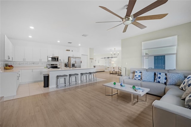 living room featuring recessed lighting, ceiling fan with notable chandelier, visible vents, and light wood finished floors