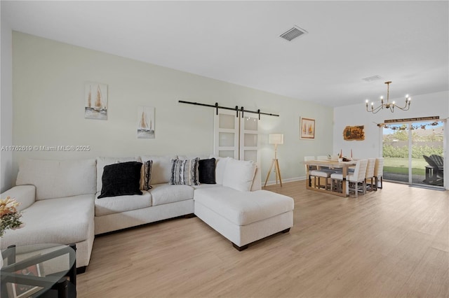 living room with a notable chandelier, visible vents, light wood-style floors, and a barn door