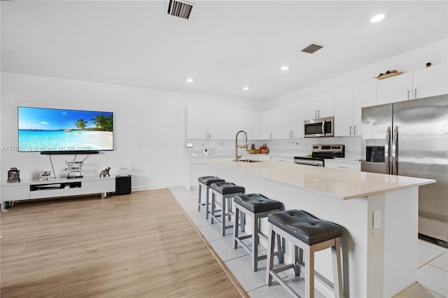 29081 SW 168th Ct, Homestead, FL 33030 - kitchen featuring stainless steel appliances, a sink, a breakfast bar area, white cabinets, and light wood finished floors