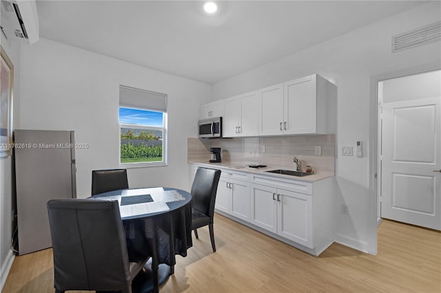 kitchen with visible vents, a sink, decorative backsplash, light countertops, and stainless steel microwave