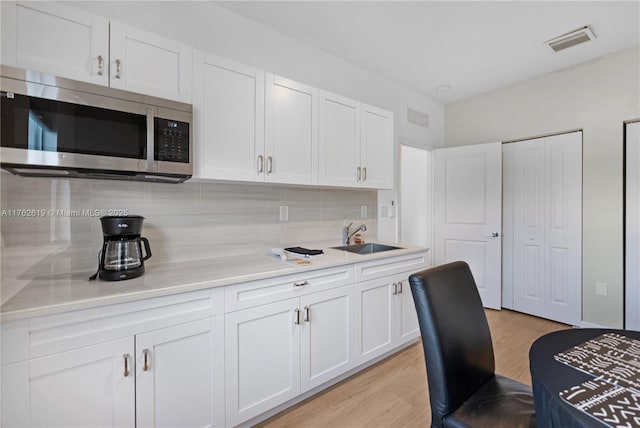 kitchen featuring tasteful backsplash, stainless steel microwave, visible vents, and a sink