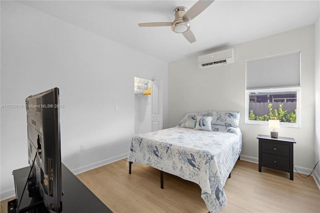 bedroom featuring a ceiling fan, light wood-style floors, baseboards, and a wall mounted air conditioner