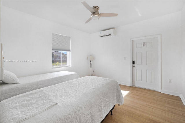 bedroom featuring a wall mounted air conditioner, light wood-type flooring, baseboards, and ceiling fan