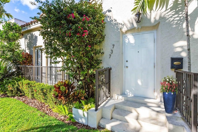 entrance to property featuring stucco siding and fence