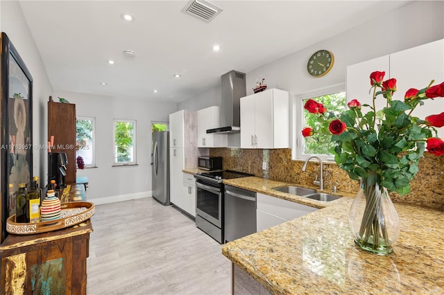 kitchen with visible vents, backsplash, wall chimney range hood, stainless steel appliances, and a sink