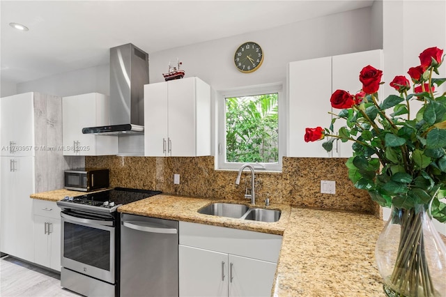 kitchen featuring backsplash, wall chimney range hood, appliances with stainless steel finishes, white cabinets, and a sink