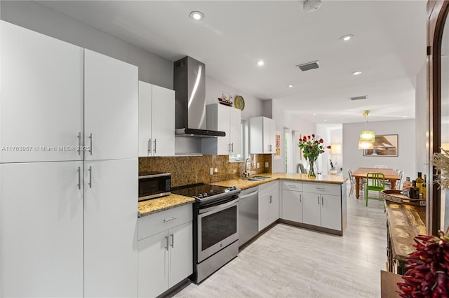 kitchen with a peninsula, a sink, appliances with stainless steel finishes, wall chimney range hood, and tasteful backsplash