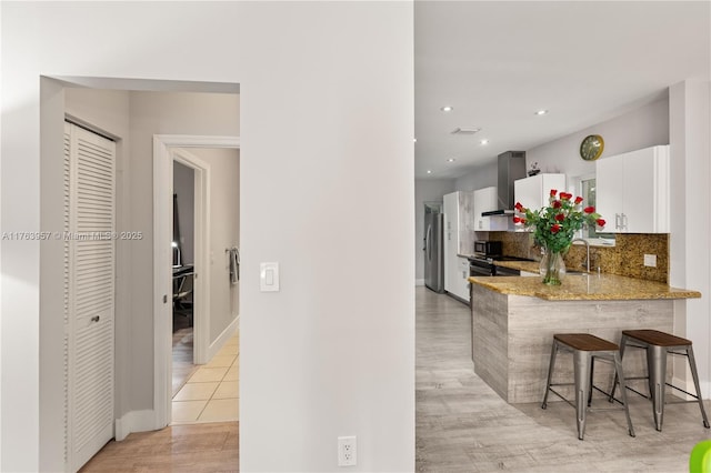 kitchen with wall chimney range hood, a breakfast bar, light stone counters, decorative backsplash, and freestanding refrigerator