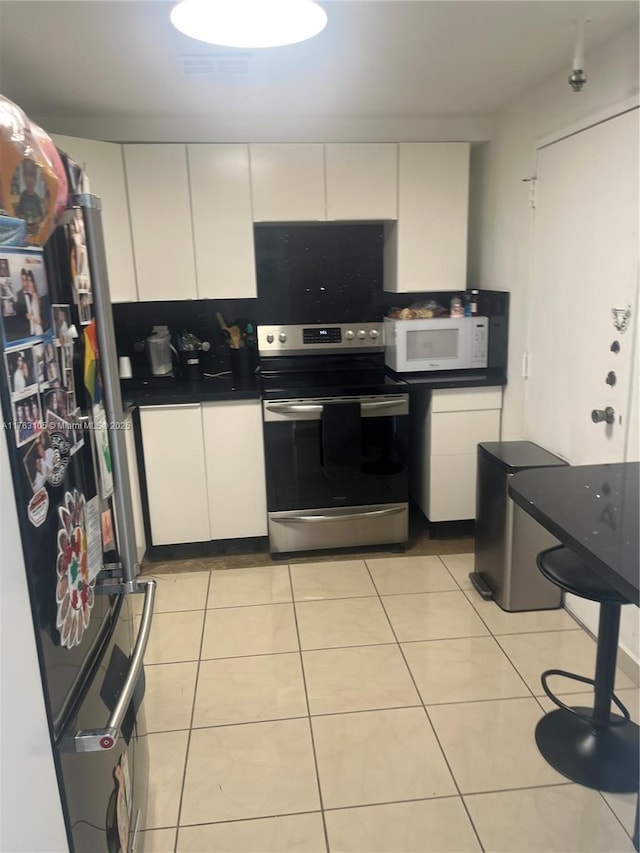 kitchen with stainless steel electric range oven, white microwave, light tile patterned flooring, and freestanding refrigerator