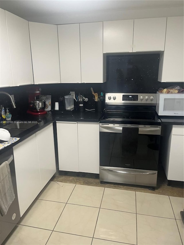 kitchen with dark countertops, light tile patterned floors, appliances with stainless steel finishes, white cabinetry, and a sink