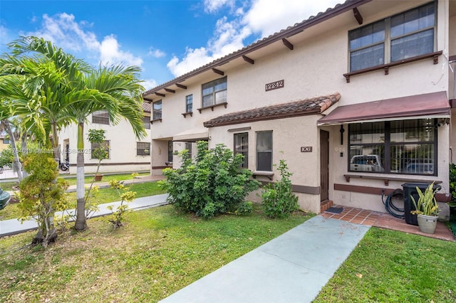 mediterranean / spanish house with stucco siding, a tile roof, and a front lawn