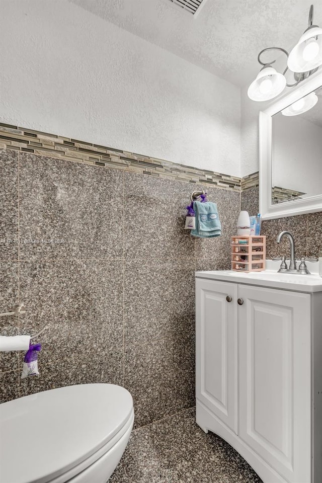 half bath featuring vanity, a textured ceiling, tile walls, toilet, and a textured wall