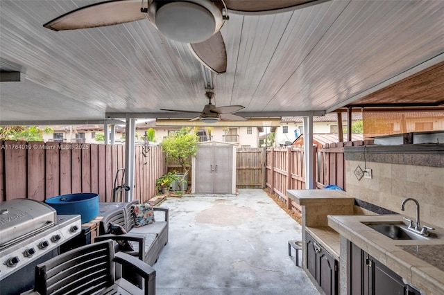 view of patio featuring a shed, exterior kitchen, a fenced backyard, a sink, and an outdoor structure