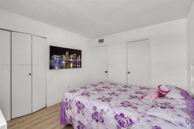 bedroom with light wood-type flooring, visible vents, and a closet