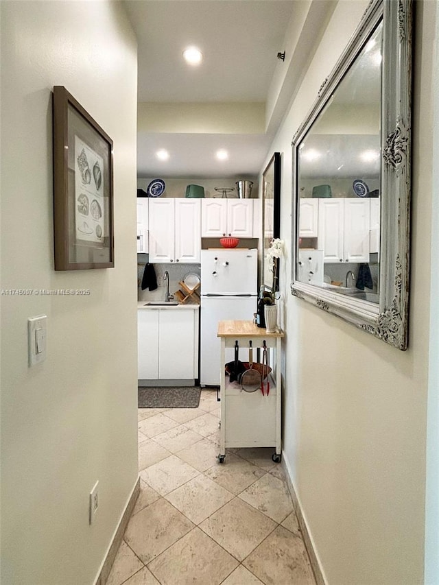 kitchen with a sink, baseboards, white cabinets, and freestanding refrigerator