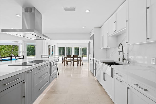 kitchen with visible vents, decorative backsplash, island range hood, black electric cooktop, and a sink