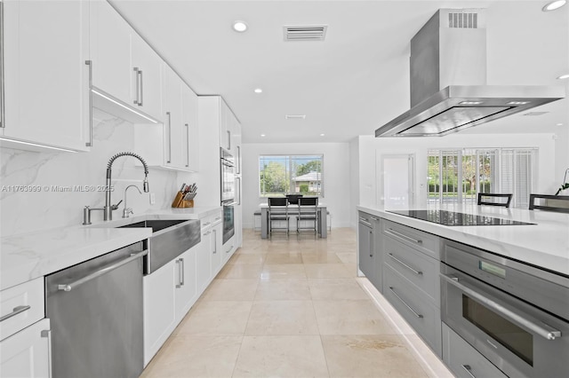 kitchen with visible vents, a sink, stainless steel appliances, wall chimney range hood, and tasteful backsplash