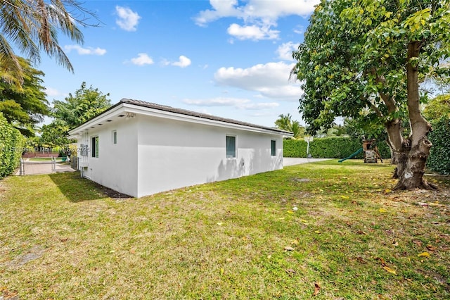 view of side of property with stucco siding, a lawn, and a playground